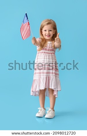 Funny little girl with USA flag showing thumb-up on blue background
