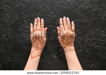 Beautiful female hands with henna tattoo on black textured background Royalty-Free Stock Photo #2098012765