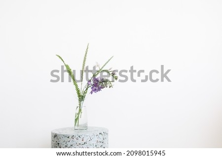 On a concrete table there are purple fresh flowers in a glass vase. The concept of interior and home items.