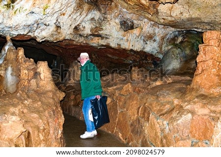 A woman, a member of a tourist group, poses against the backdrop of a cave.