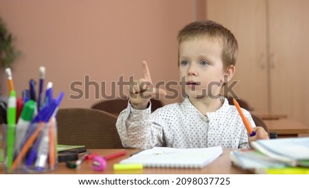 A handsome three year old boy sits at his desk in the class and thinks about the answer.