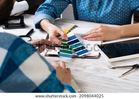 Designers discussing color palette at desk. Creative workspace with color swatches and tablet computer. Professional interior designing. Coloristics and product branding in visual design studio.