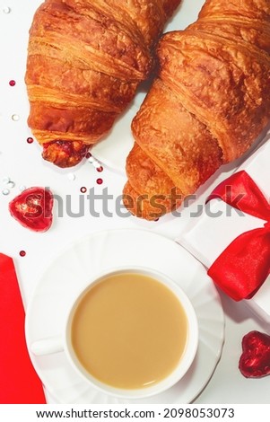 A romantic breakfast for a loved one on Valentine's Day. Fresh delicious croissants for breakfast with a cup of coffee, chocolate hearts, present on white table. French puff pastries with coffee.