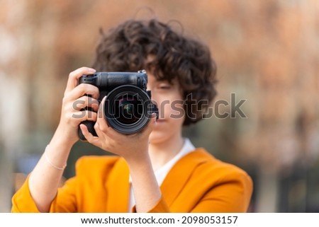 Young brunette woman with curly hair taking a picture with her big camera