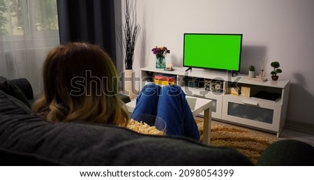 Woman Sitting on a Couch Home Watching Green Chroma Key Screen, Relaxing. Girl in a Cozy Room Watching Sports Match, News, Sitcom TV Show or a Movie on Green Screen eating popcorn.