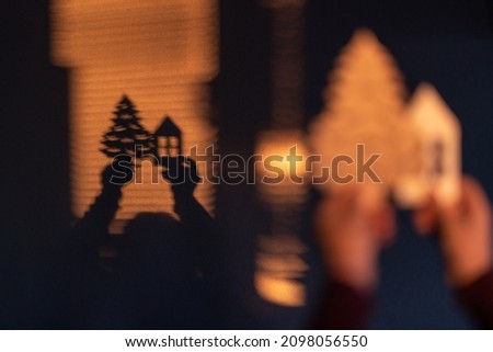 Shadow play. Hands holding a wooden tree and a house and their shadows are reflected on the wall. Selective focus