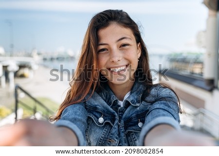 Cute, positive teenager holding a camera, looking straight. Beautiful girl sincerely smiling on the background of the city