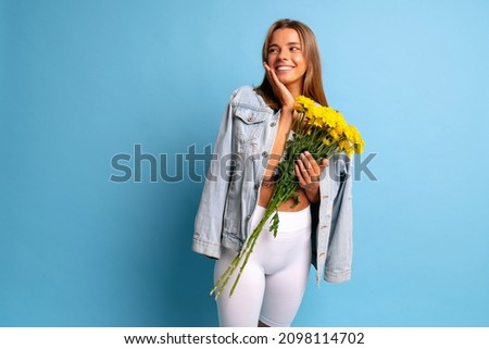 Cute blonde woman posing at blue background with big bouquet of yellow flowers, spring time.