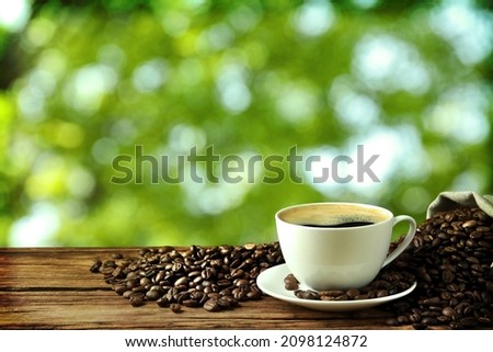 Cup of aromatic hot coffee and beans on wooden table outdoors. Space for text