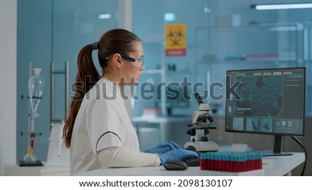 Chemist with protective goggles and gloves working on computer to analyze dna animation for biology development. Woman looking at monitor with scientific diagnosis illustration.