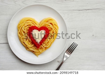 Heart shaped spaghetti with tomato sauce and parmesan cheeses on white plate with white wood background.Romantic vegetarian art food idea for Valentine's dinner.Top view.Copy space