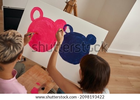 Cropped image of young lesbian girls painting picture of mouse heads with pink and purple paints at home. Domestic entertainment, hobby and leisure. Homosexual relationship and spending time together