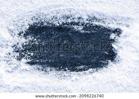 Wiped clear space of dark blue ice on a snowy surface of a frozen winter river.