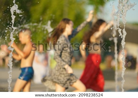 Defocused photography in silhouettes. Children playing with water of fountain. They are having fun. Hot summer amusement. Lifestyle concept.