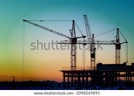 Construction cranes are building a house against the background of sunset and dark sky Royalty-Free Stock Photo #2098269895
