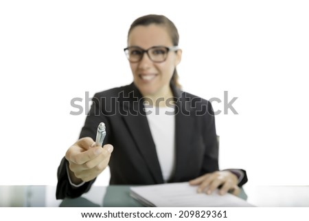 young business woman offering a pen to sign a document sitting on a desk - focus on the pen