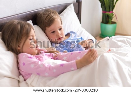 Little Preschool Toddler Minor Children Siblings Kids Watch Cartoon Use Smartphone Phone Device Together. Baby In Pajama On White Bed At Home Bedroom. Family, Leisure, Childhood, Friendship Concept