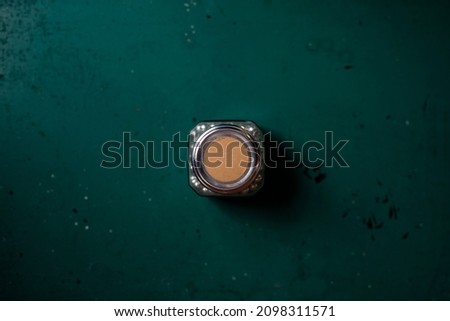 Glass containers holding office supplies with rustic brown blank label on top. Overhead flat-lay shot of container on rustic green wood surface naturally lit.