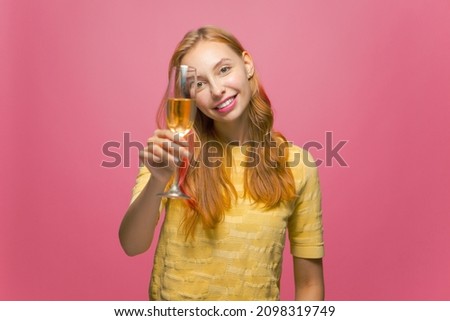 Beautiful happy female celebrating holiday holding glass of champagne, smiling, congratulating on pink studio background