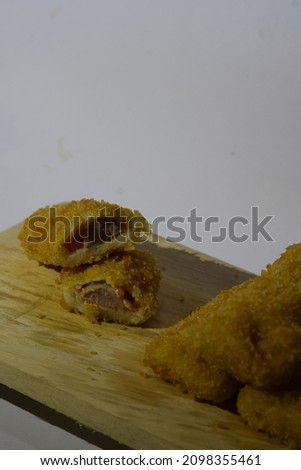 Two pieces of delicious fried risoles from Indonesia containing sausage, mayonnaise and sauce. White background and wooden table. 