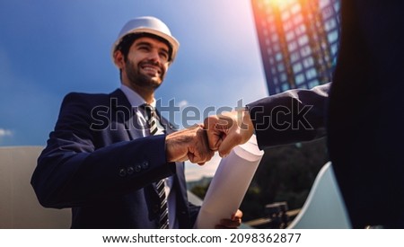 Two successful real estate project development male engineers stand in front of a large condominium project. Concept of good business cooperation or partnership.