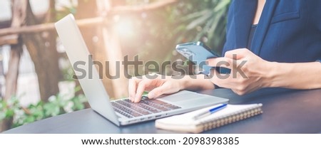Woman working with a laptop computer and uses a cell phone in the office.Web banner.