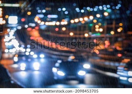 Blurry lights of moving cars and lanterns reflecting on the wet asphalt in the night city in rain. Rainy bad weather concept.