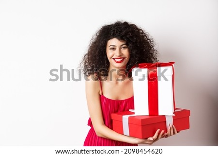 Beautiful birthday girl with curly hair, holding bday gifts and smiling happy, celebrating, standing against white background
