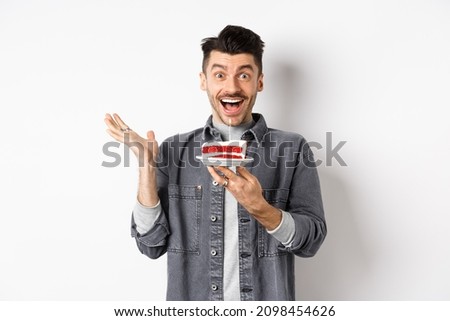 Excited man celebrating birthday, looking happy, holding cake with candle, making wish, standing happy against white background
