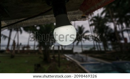 A dim light bulb with a swimming pool, coconut trees and beach in the background