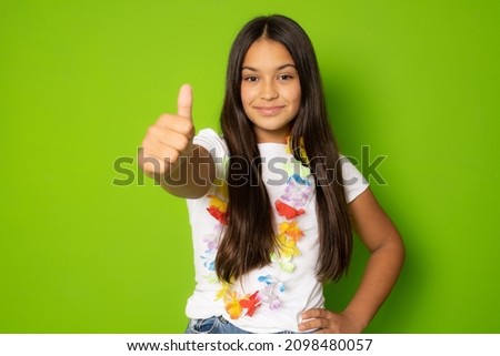 Brunette hispanic girl in casual clothing showing thumb up isolated over green background.