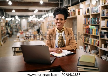 Happy African American female professor holding online class from university library and looking at camera. 