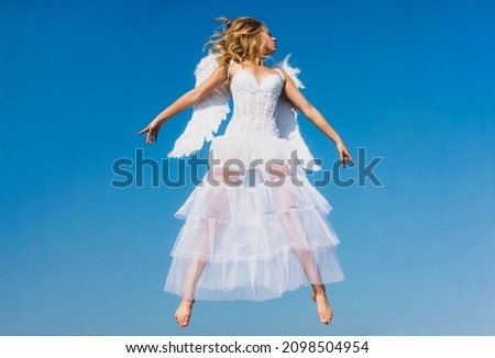 Valentines Day. Cupid girl with white wings. Woman with angel wings with bow and arrow against blue sky. Flying angel.