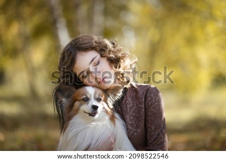 Portrait of a blonde girl with a small dog in the autumn forest