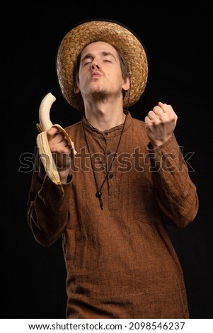 Young handsome tall slim white man with brown hair blown away by the taste of banana with brown shirt on black background