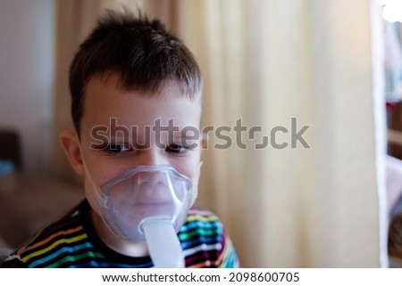 Child holds a mask vapor inhaler. Sick Caucasian boy using inhaler containing medicine to stop coughing from disease. Little boy making inhalation with nebulizer. Treatment of bronchitis and pneumonia