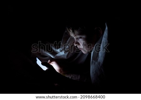 kid who plays games on the internet at night. Portrait of a teenager boy using mobile phone on dark bed. High quality photo. Bad habits of teenagers. Boy addicted with phone. Royalty-Free Stock Photo #2098668400