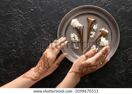 Woman holding tray with henna paints and flowers on black textured background