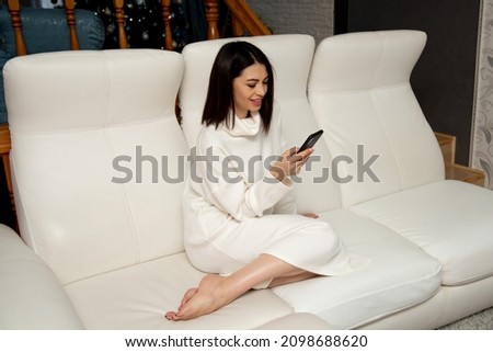 A beautiful girl sits on a white sofa and talks on the phone. Communication. Communication.