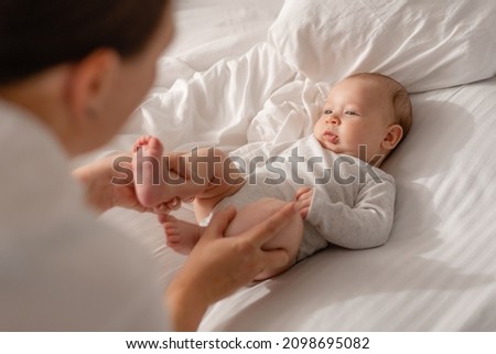 mom plays with the baby, gives him a massage, teaches him to sit down and control his body. child in a white bodysuit on a white bed. healthy active kid. lifestyle. space for text. High quality photo