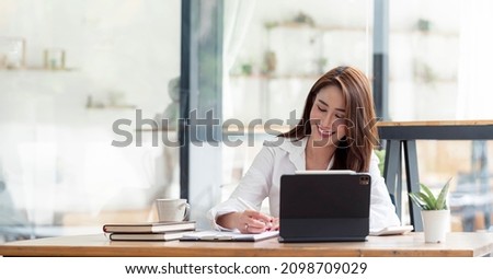 Photo of cheerful pretty asian woman having been employed to job as executive smiling toothily sitting at desktop with laptop and writing note. Royalty-Free Stock Photo #2098709029