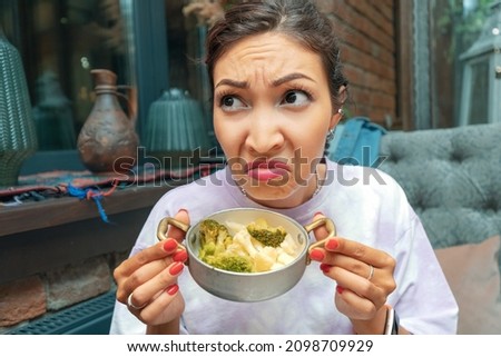 A disgruntled woman face with cauliflower and steamed broccoli. The concept of a boring diet and eating disorders