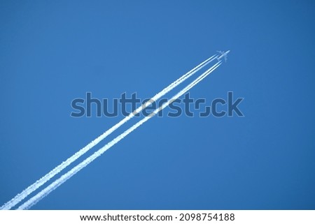 Large four engine passenger supersonic aircraft flying from left to right high in clear blue cloudless sky leaving bright long white trail Royalty-Free Stock Photo #2098754188