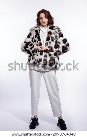High fashion photo of a beautiful elegant young woman in a pretty leopard print fur coat, trousers, pants posing over white background. Make up, hairstyle. Slim figure. Studio shot