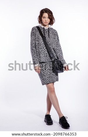 High fashion photo of a beautiful elegant young woman in a pretty gray leopard print blouse, skirt, black handbag posing over white background. walking style. Make up, hairstyle. Slim figure.