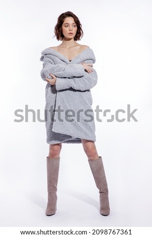 High fashion photo of a beautiful elegant young woman in a pretty pale blue fur coat, suede boots posing over white background. Make up, hairstyle. Slim figure.