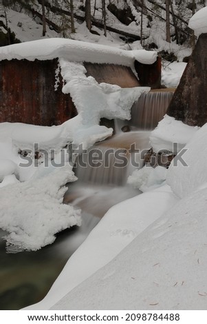Artificial cascade on the creek. Snowy and frozen waterfall. Slow shutter speed.  Motion photography. Ice icicles.