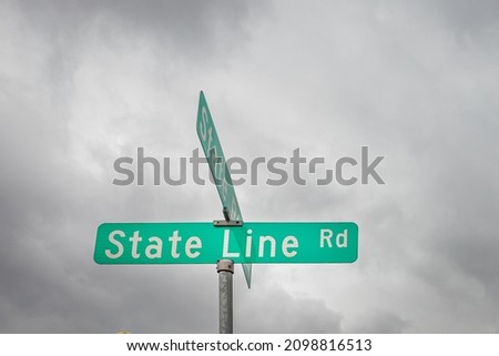 A street sign denoting a road that runs along a state line.