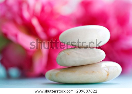 Close up still life detail view of a pile of natural smooth white stones balancing in a stack against bright pink blossom flowers in a health spa background, interior. Nature objects and zen energy.
