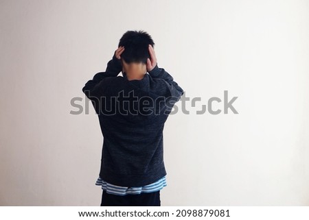 Back view of young boy stands and close his ears with hands, faces to the wall. Concept :  Depression , anxiety disorder angry, disobey, don't want to hear, naughty kid.                Royalty-Free Stock Photo #2098879081